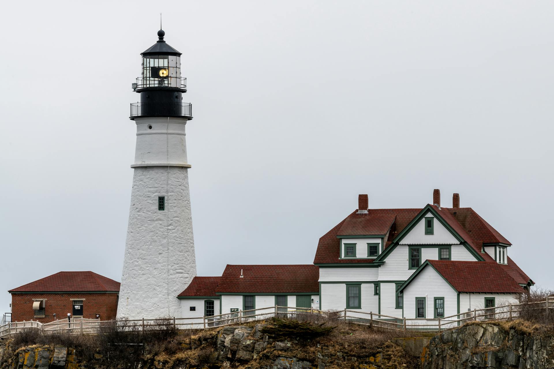 White lighthouse and aged residential houses against cloudy sky