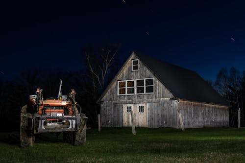 Tractor parked in meadow near shed in farm at night