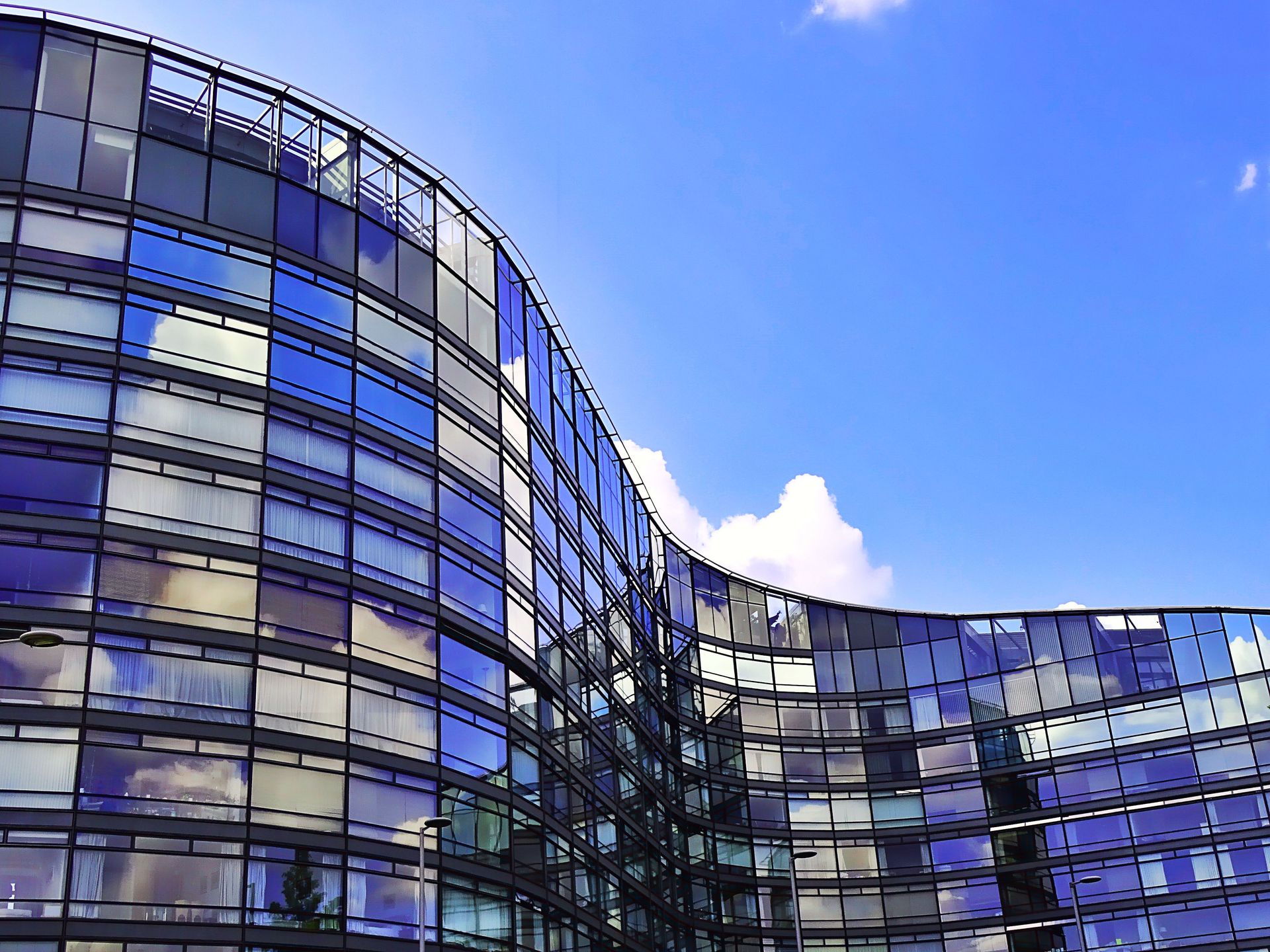 Curved architecture with glass panels reflecting the sky and clouds, showcasing modern design.