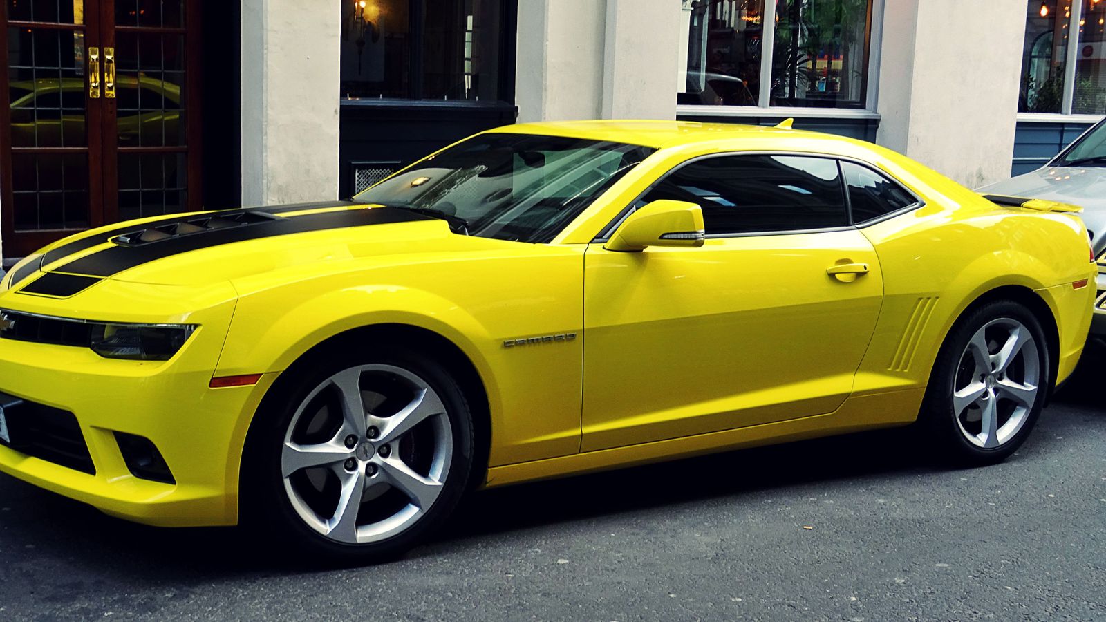A yellow Chevrolet Camaro parked on a city street, a real stock photo with no people in the frame, chosen because Bumblebee, the best-known Autobot, takes a Camaro form in the live-action Transformers films. It is not a still from any movie
