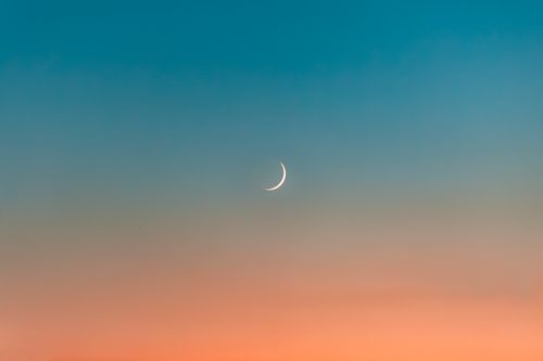 Free A serene crescent moon set against a vivid gradient sky at sunset, exuding tranquility. Stock Photo