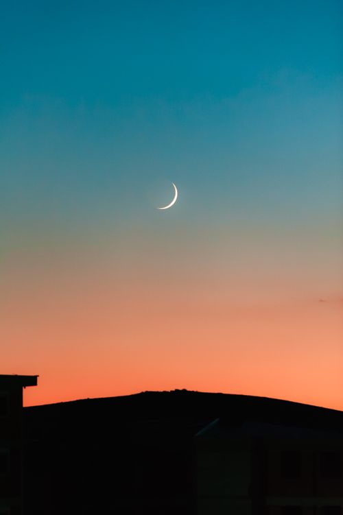 Free Dramatic crescent moon above mountain silhouette during a vibrant sunset sky. Stock Photo