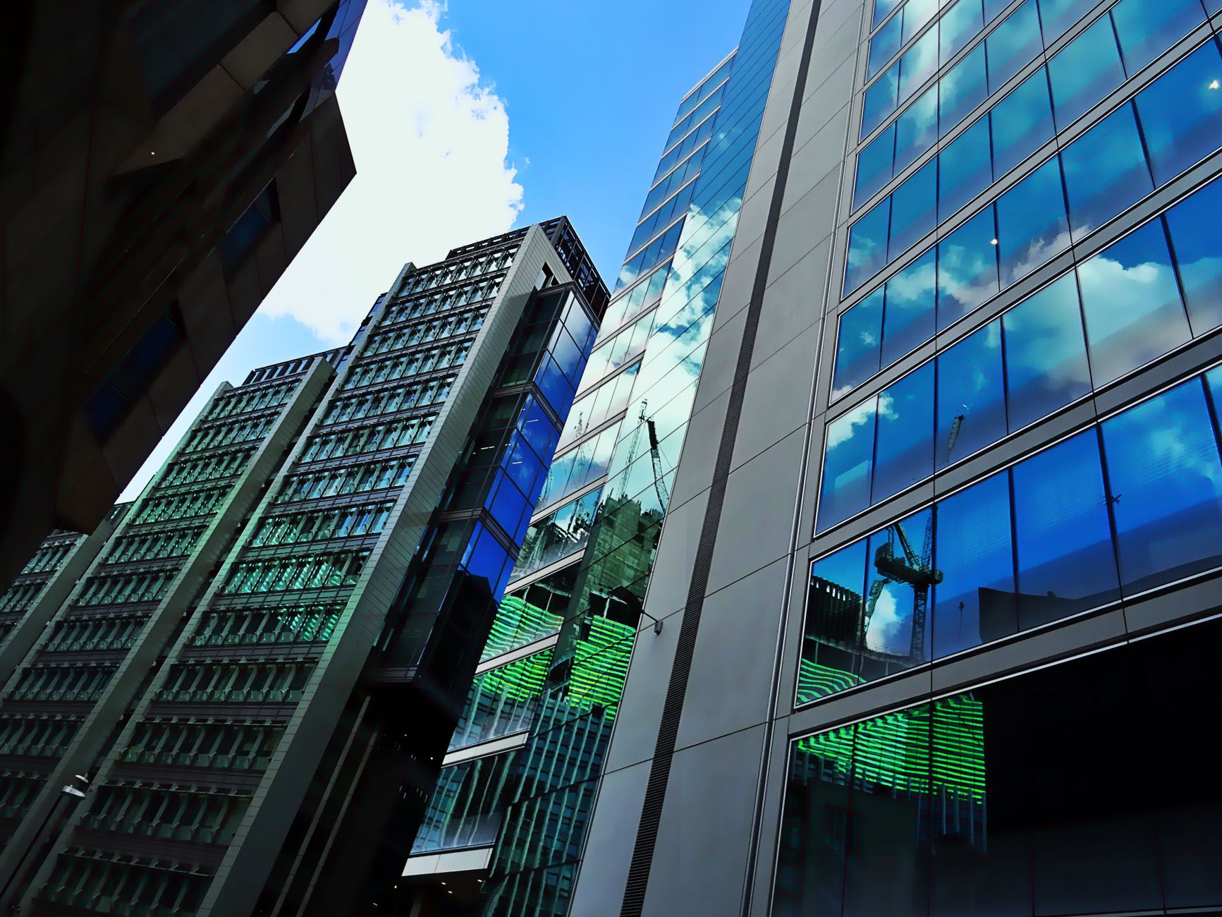 Low angle view of modern skyscrapers with glass facades reflecting blue sky and clouds.