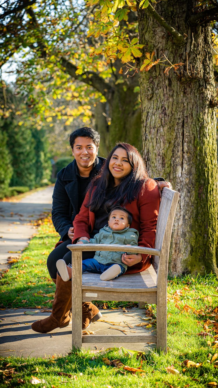 Positive Ethnic Family With Toddler On Bench In Sunny Park