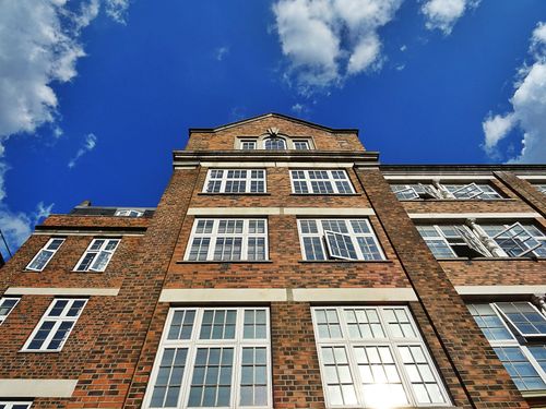 Free A captivating low angle perspective of a brick building with windows against a vibrant blue sky and clouds. Stock Photo