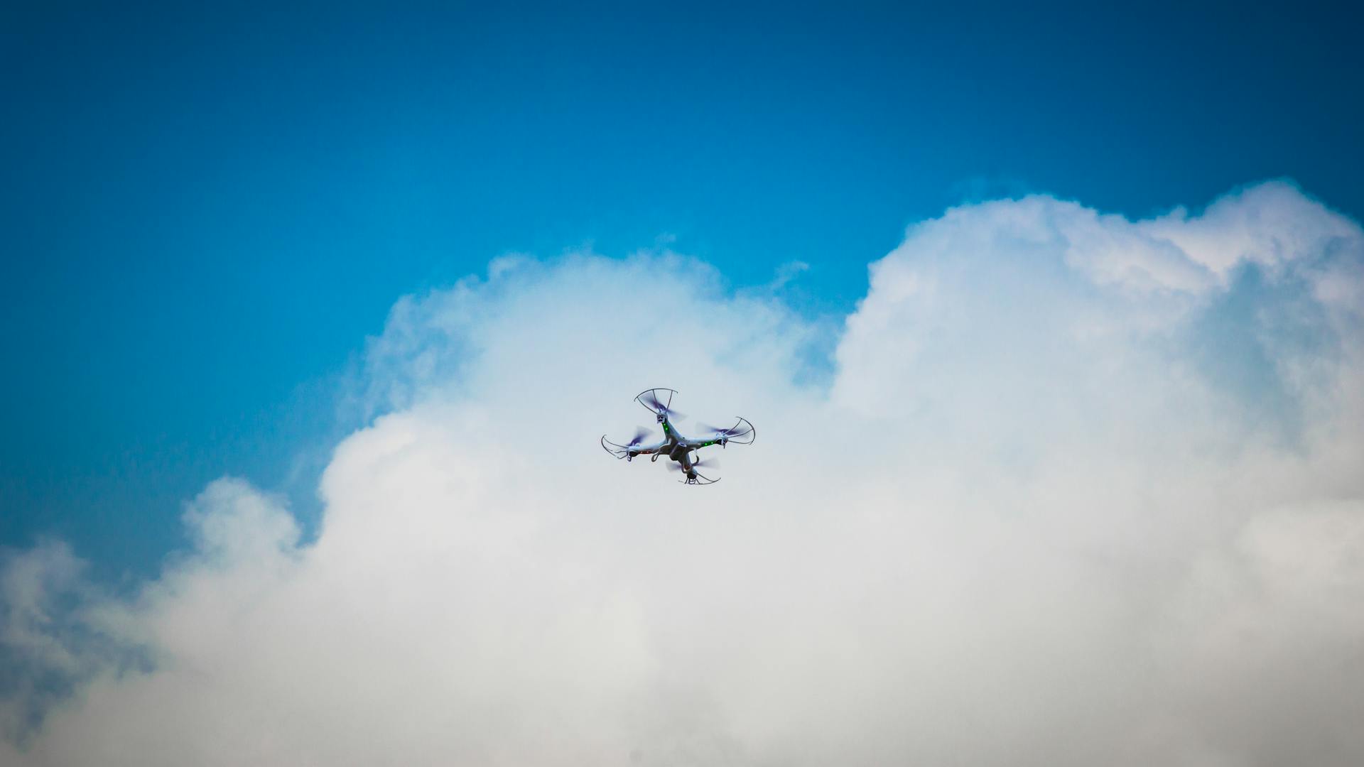 Drone flying against a vibrant blue sky with fluffy clouds, showcasing modern technology