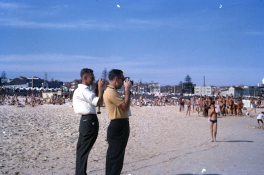 Two photographers capturing a vibrant day at a bustling beach filled with sunbathers.