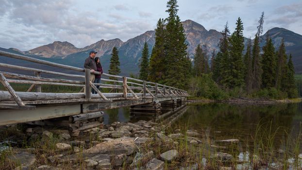 A couple enjoys a serene moment on a wooden bridge at Pyramid Lake, Alberta, surrounded by nature.