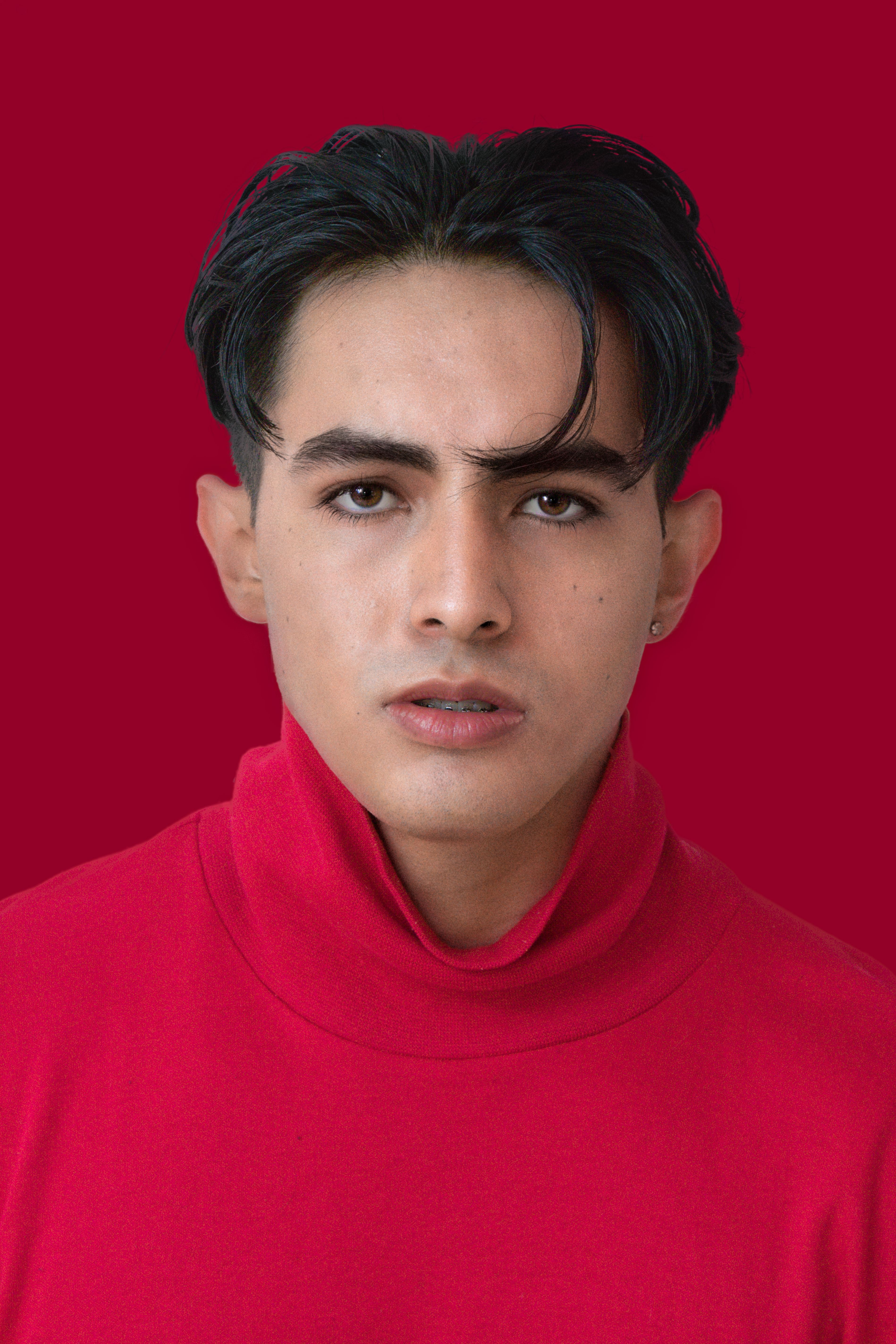 Confident young man in a vivid red turtleneck against a red background, exuding style and charisma.