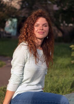 A cheerful woman with curly hair enjoys a sunny day outdoors in casual attire.