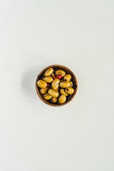 A bowl of marinated green olives with red pimientos on a white background.