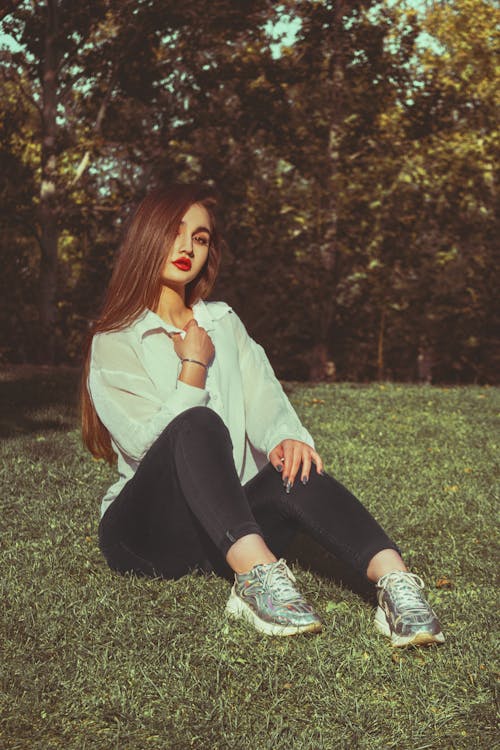 Woman in White Long Sleeve Shirt and Black Pants Sitting on Green Grass Field