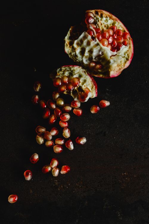 Free A vibrant pomegranate with scattered seeds on a dark backdrop, highlighting natural beauty. Stock Photo