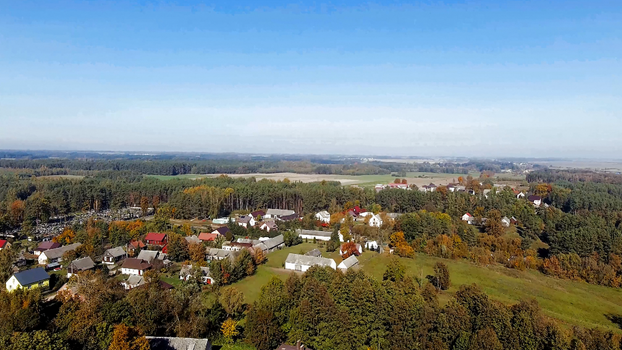 Scenic aerial view of a rural village surrounded by autumn trees and open fields under a clear blue sky.