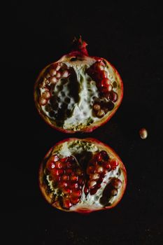 A moody and artistic image of a halved pomegranate showcasing seeds on a dark background.