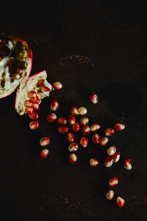 Free A dark minimalist shot of scattered pomegranate seeds, highlighting their vibrant color and fresh appeal. Stock Photo