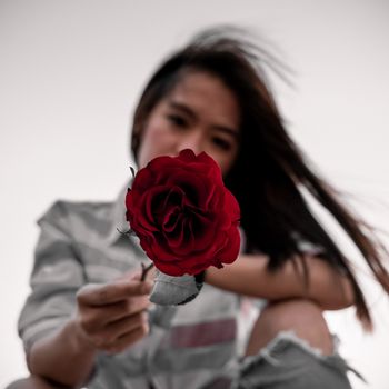 一个女人手拿一朵充满活力的红玫瑰，在户外营造出平静而浪漫的氛围