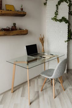 A minimalist home office setup with a glass desk and laptop, perfect for remote work.