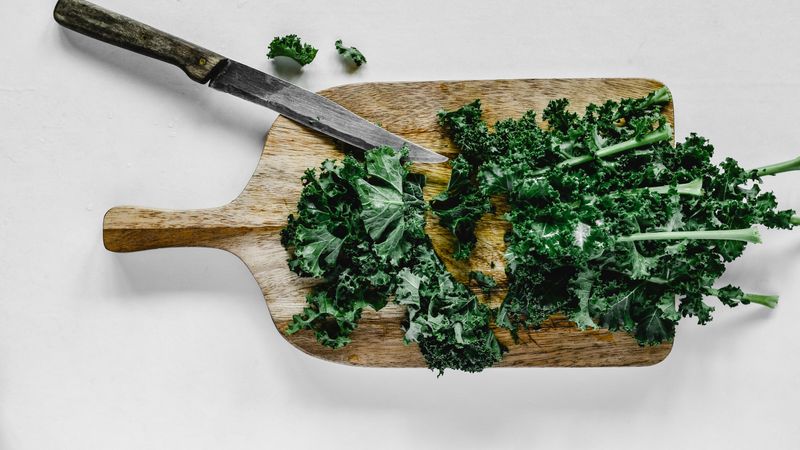 person feeding chopped kale into a slow juicer on a kitchen counter