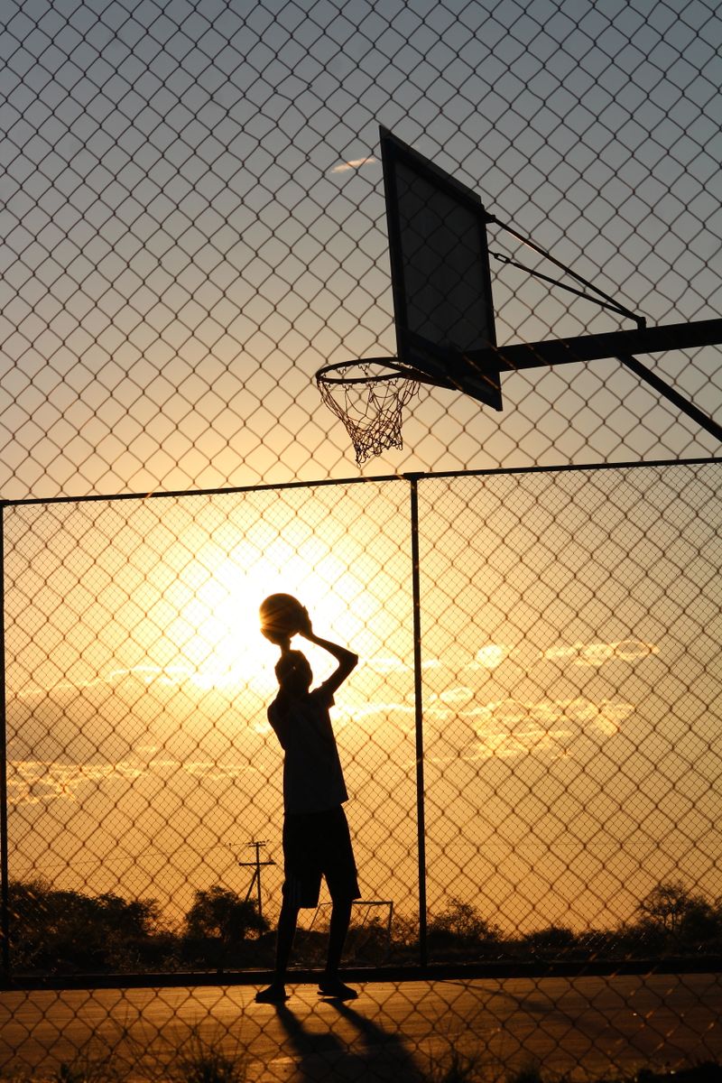 Silhouette of a basketball player at an outdoor hoop during sunset