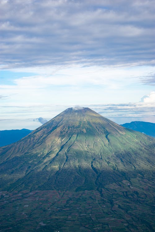 Majestic landscape of volcanic mountain peak with grassy slopes in valley under sunlight