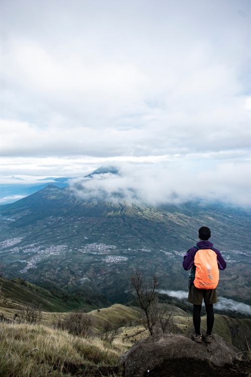 Free Back view of anonymous man with backpack standing on hill and admiring picturesque scenery of mountain ridge in cloudy weather Stock Photo