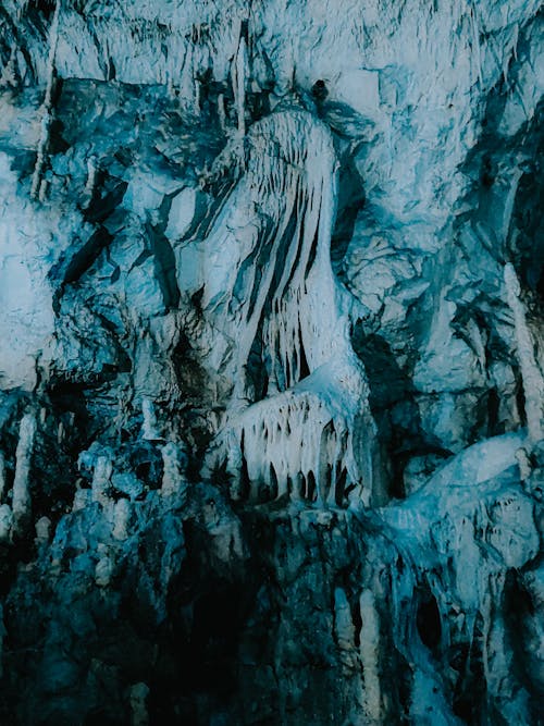 Icicles hanging on rough surface of rocky formation in dark cave in winter