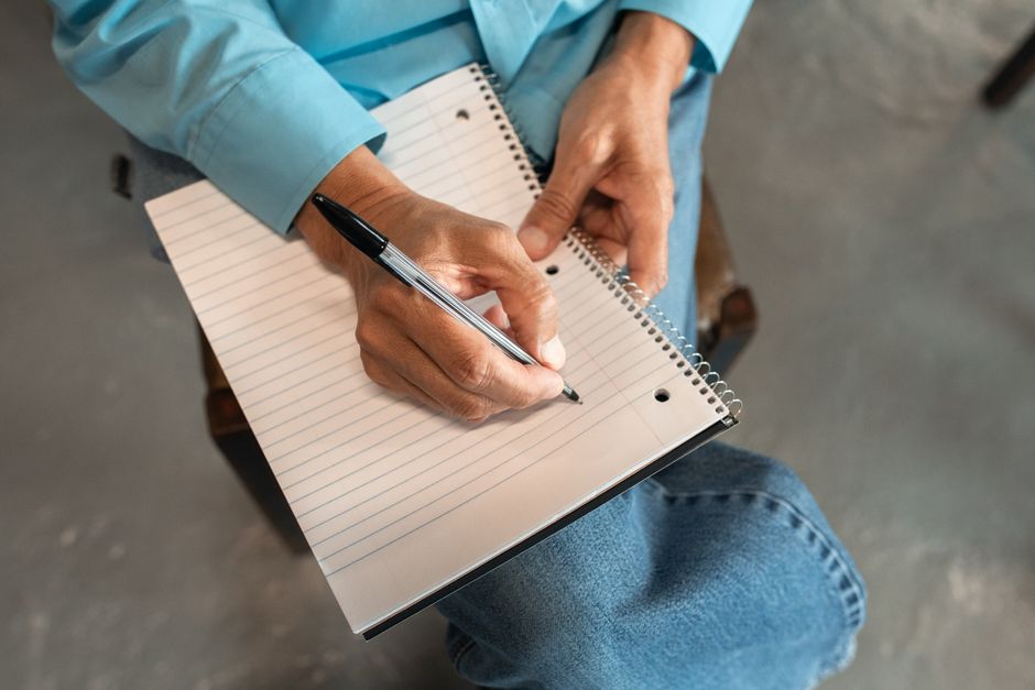 A person hand-writing SMART goals in a notebook with a coffee nearby - monthly progress tracking plan A person hand-writing SMART goals in a notebook with a coffee nearby - monthly progress tracking plan