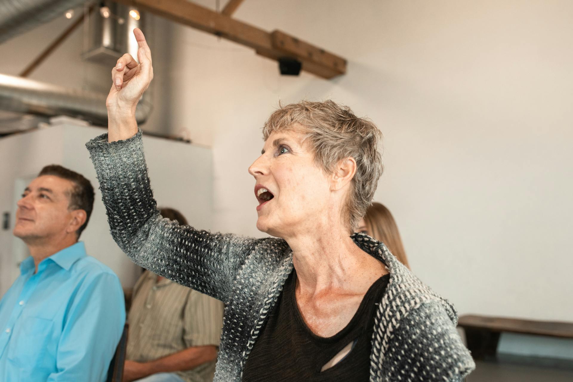 Senior caucasian woman attentively pointing during indoor seminar with diverse audience.