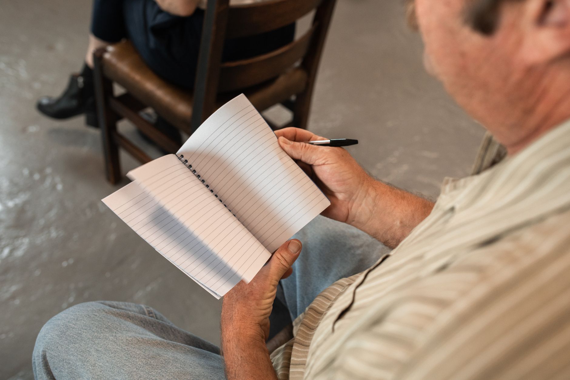 A man writing in a notebook during an indoor meeting or discussion.