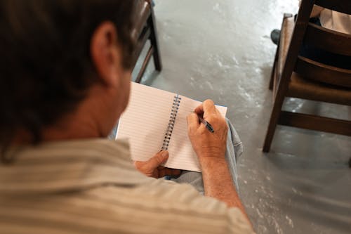 A Person Writing on a Notebook Using a Pen