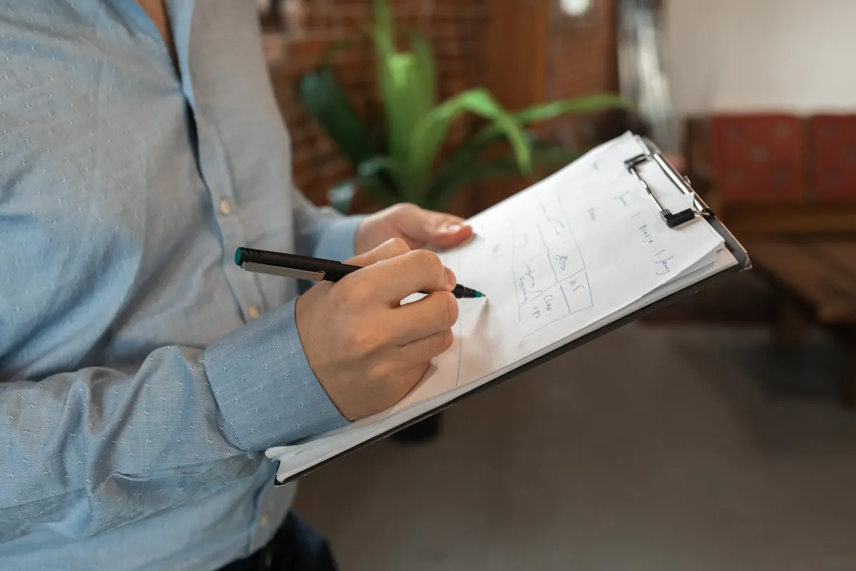 A person in a blue shirt holding a clipboard and working through a handwritten checklist with a marker.