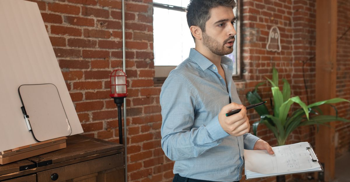 Um jovem está em um loft com paredes de tijolo ensinando ou apresentando com um clipboard e caneta.
