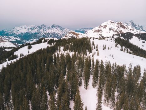 Breathtaking aerial view of snowy mountains and evergreen trees in Austria during winter.