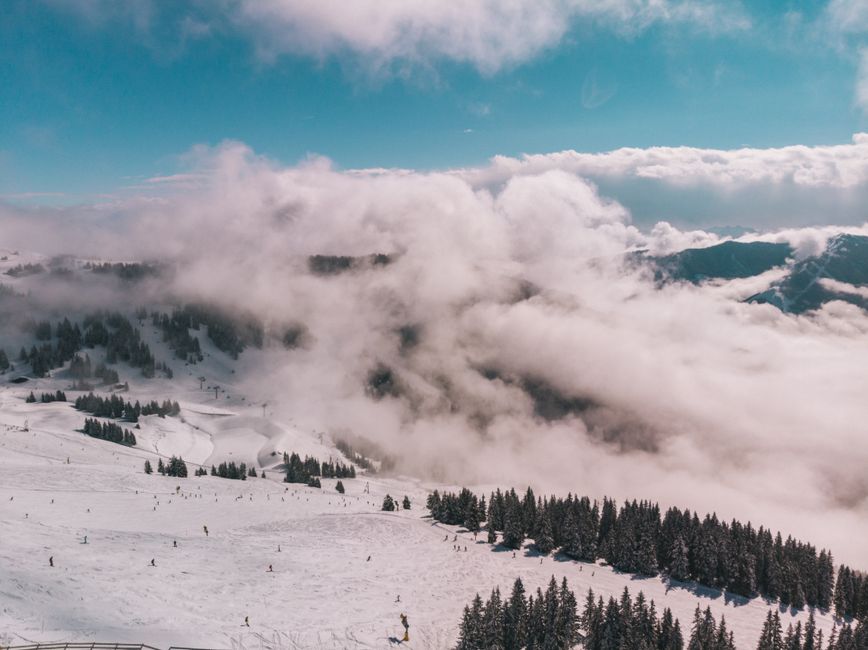 Scenic aerial shot of snow-covered mountains and skiing in Austria with cloudy skies.