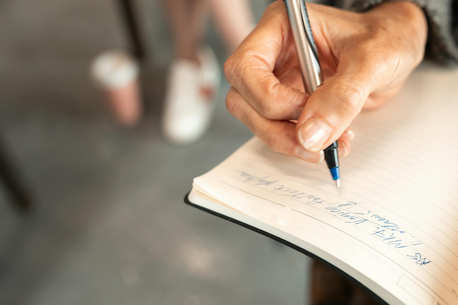 Hand Holding a Pen Writing on a Notebook