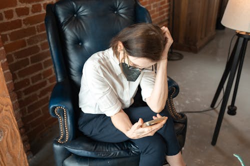 Free A Woman Sitting on an Armchair Using Her Smartphone Stock Photo