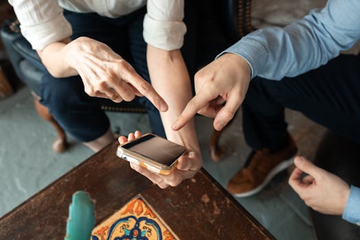 Two people engaged in discussion, pointing at a smartphone on a table indoors.
