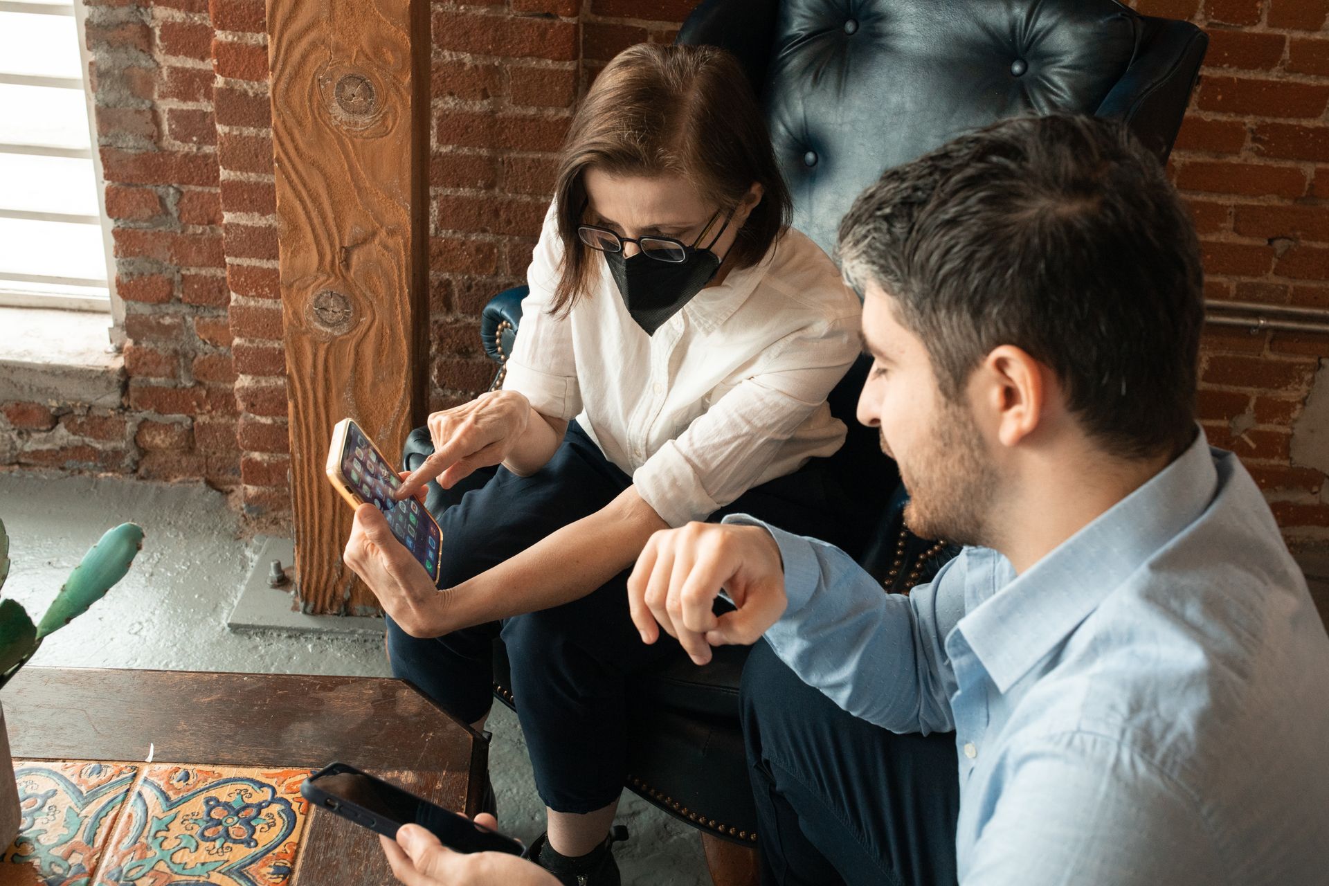 Two adults conversing and sharing content on smartphones in a relaxed, indoor office environment.