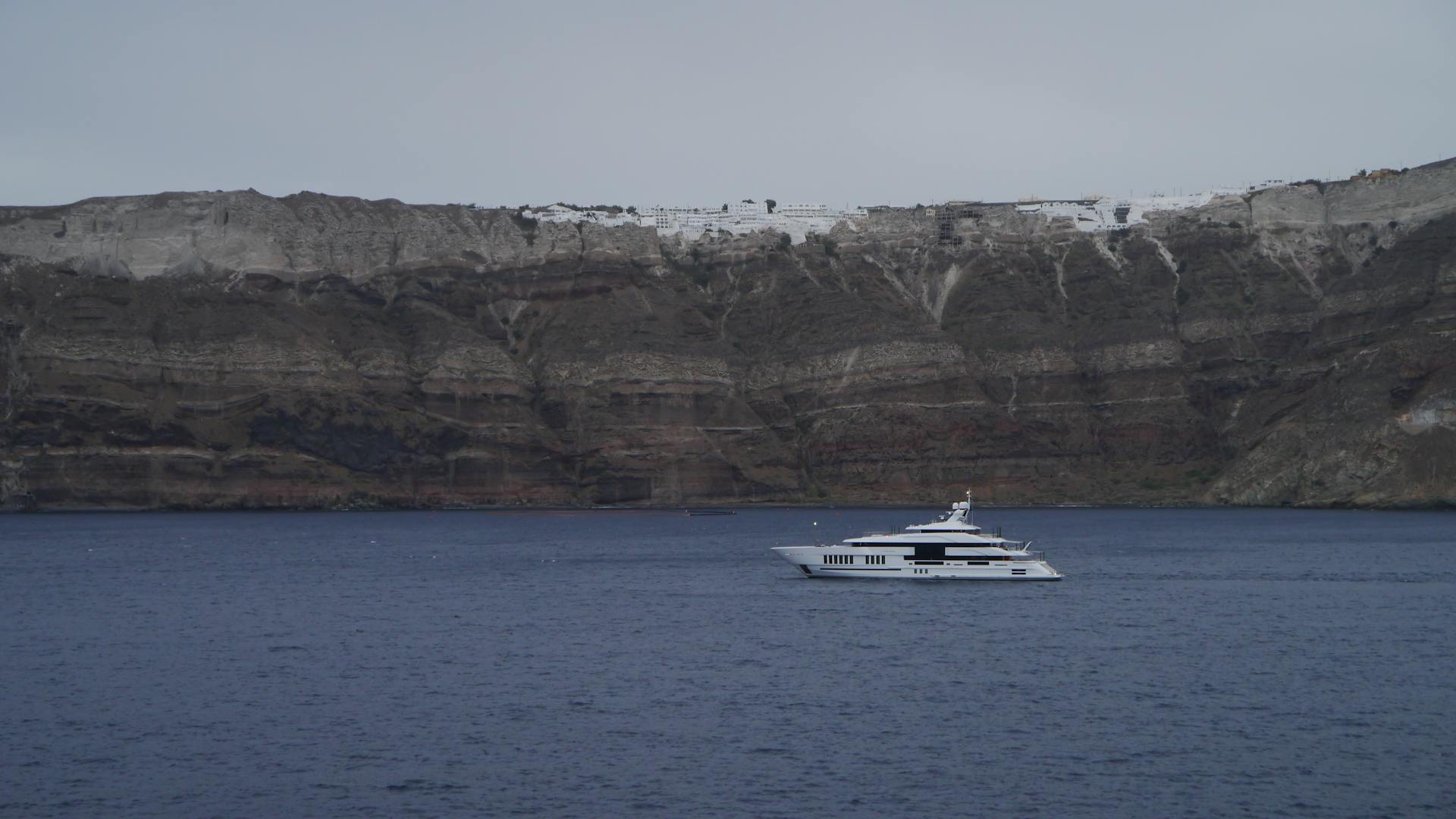 A luxury yacht cruises by the stunning cliffs of Santorini, Greece under a clear sky.