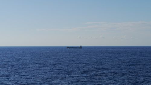 Free A tranquil scene of a bulk carrier ship cruising across a vast, open ocean under a clear blue sky. Stock Photo