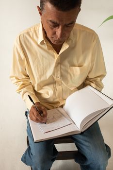 一位穿着黄衬衫的成年男子正坐在室内用笔记本做笔记
