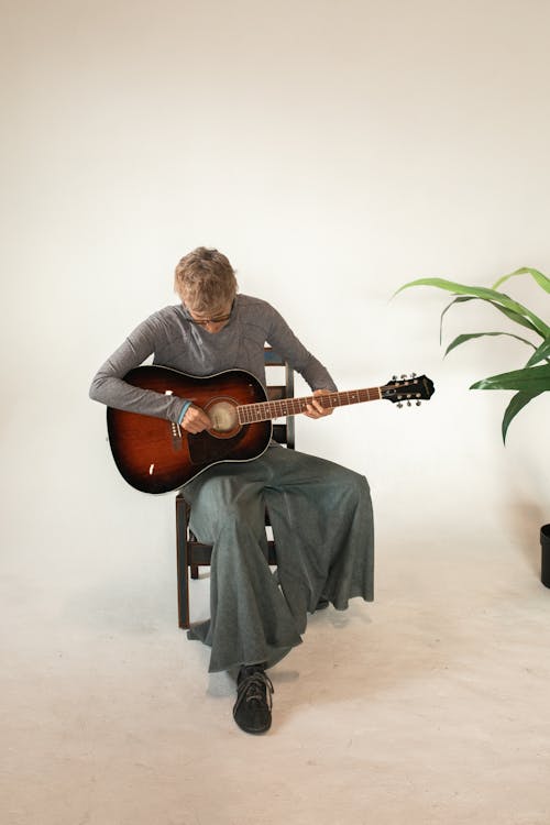 Pria Berkemeja Hitam Lengan Panjang Memainkan Gitar Akustik Coklat