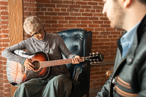 Mężczyzna W Czarnej Koszuli Gra Na Gitarze Akustycznej, Siedząc Na Czarnej Skórzanej Kanapie