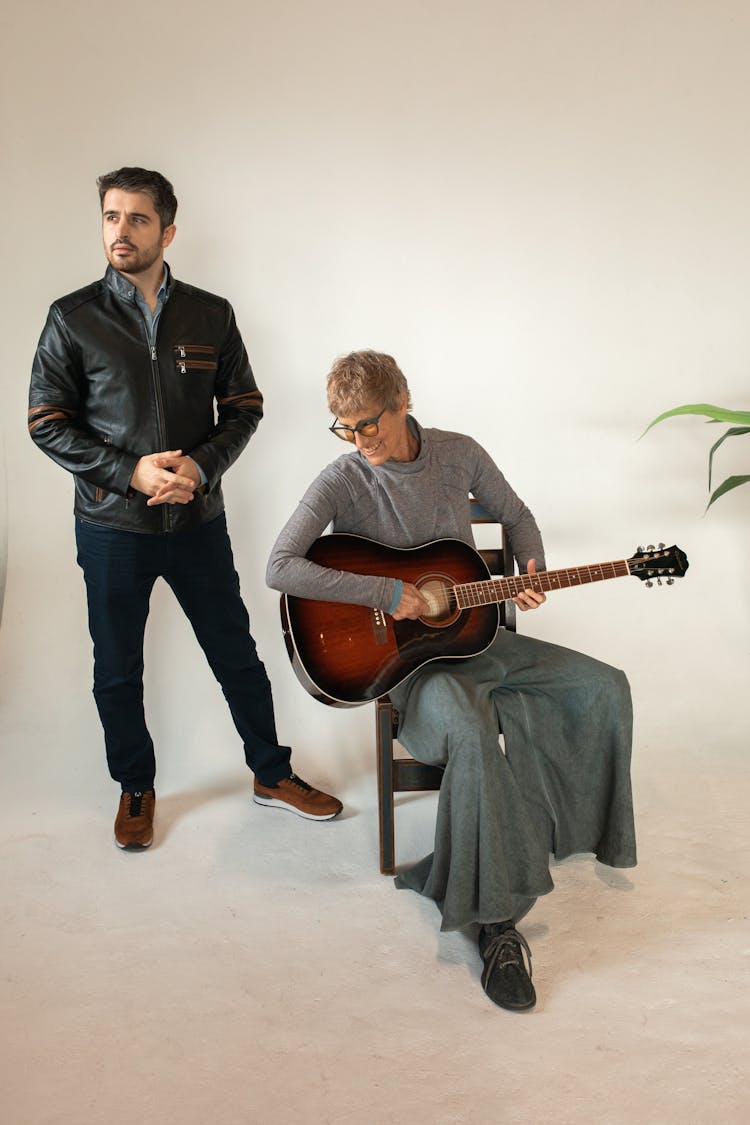 A Standing Man Beside A Seated Woman With Guitar