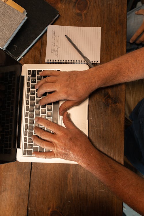 Person Using Silver Laptop on Brown Wooden Table