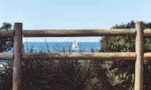 宁静的海景中，一艘帆船被质朴的木栅栏和沿海植被环绕