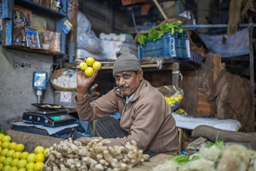Free Adult Indian man in warm clothes selling bright lemons while owning small local stall with fruit and vegetable Stock Photo