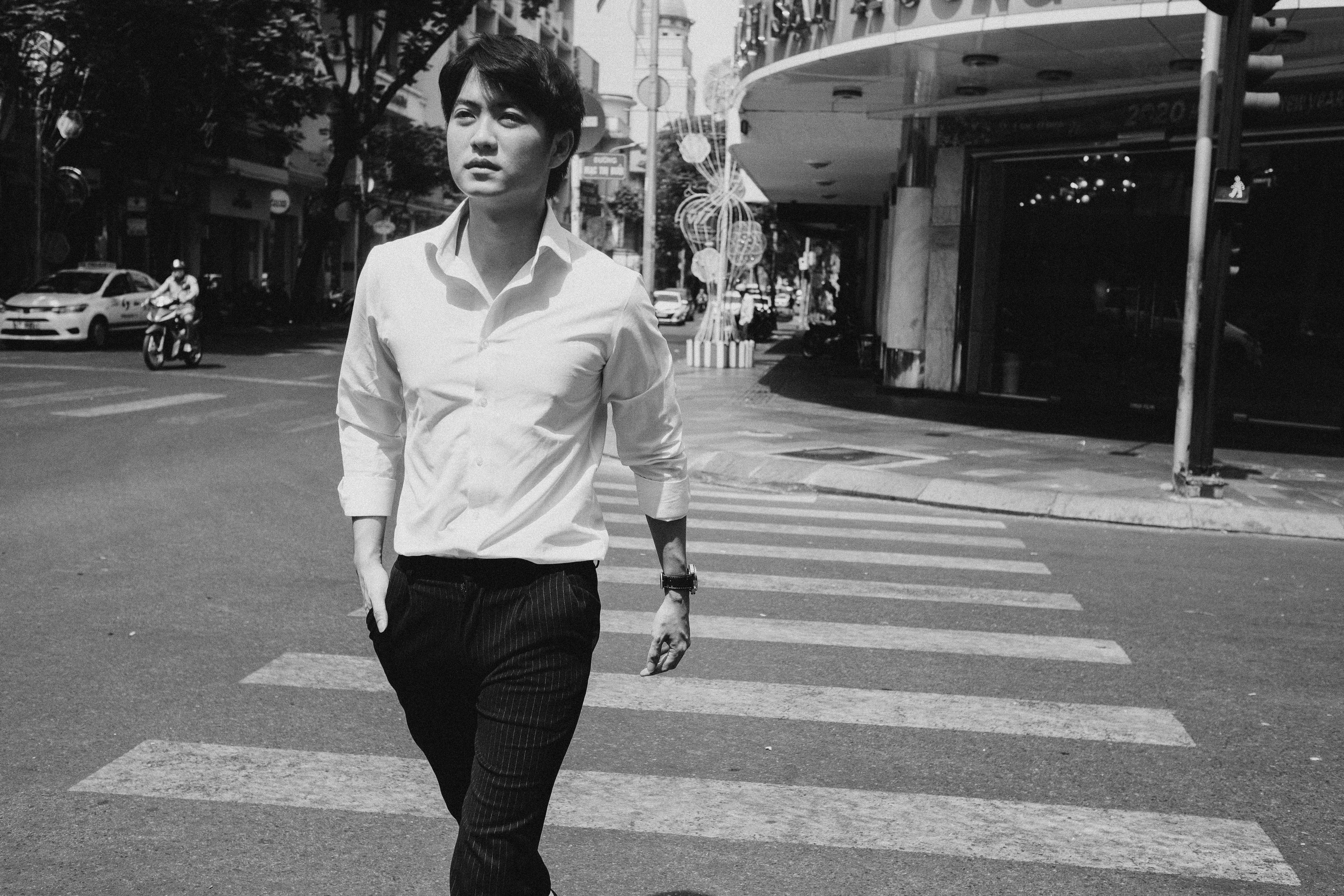 Black and white of young serious ethnic male in formal outfit walking on zebra crossing in downtown on sunny day