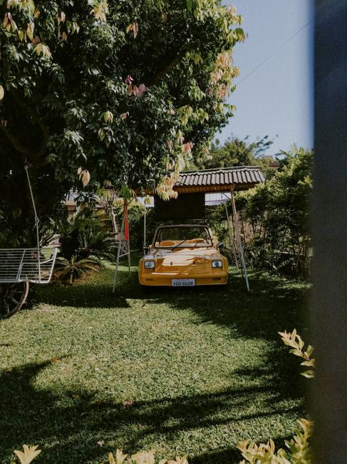 Yellow vintage car under roof on green meadow in yard of house in summer time